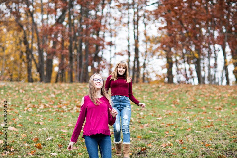 Fototapeta premium two young beautiful happy teenager girls, sisters and friends playing, running, jumping in forest. Colorful Fall, Autumn