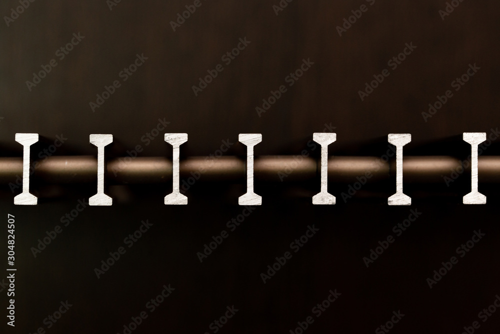 Abstract background in the form of slices of metal of a T-shaped profile and horizontal lines on a light background close-up. Abstract background in the form of slices of metal of a T-shaped profile and horizontal lines on a light background close-up.