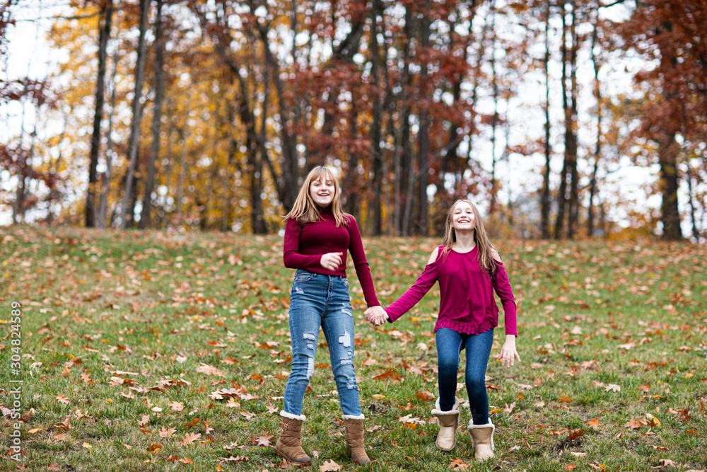 Fototapeta premium two young beautiful happy teenager girls, sisters and friends playing, running, jumping in forest. Colorful Fall, Autumn