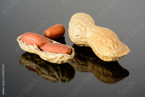 Peanut on glossy black surface with reflection. Whole peanut and open shell with two kernels macro close-up, high resolution full depth of field.