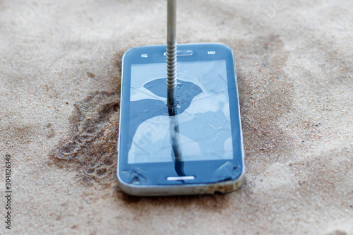 smartphone lies in the sand. a nail is driven into it. close-up. photo