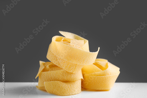 Uncooked pappardelle pasta on white table against dark grey background photo
