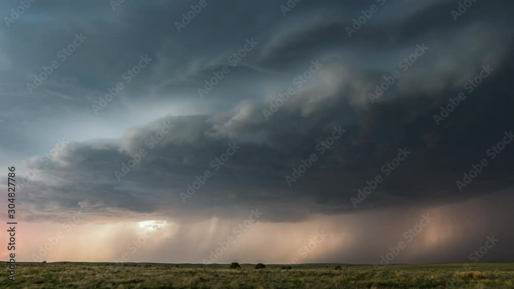 Lightning flashing through storm clouds moving over the landscape at sunset.