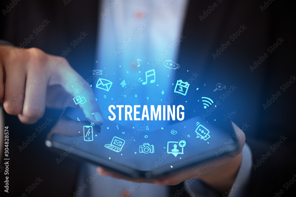 Businessman holding a foldable smartphone with STREAMING inscription, social media concept Businessman holding a foldable smartphone with STREAMING inscription, social media concept