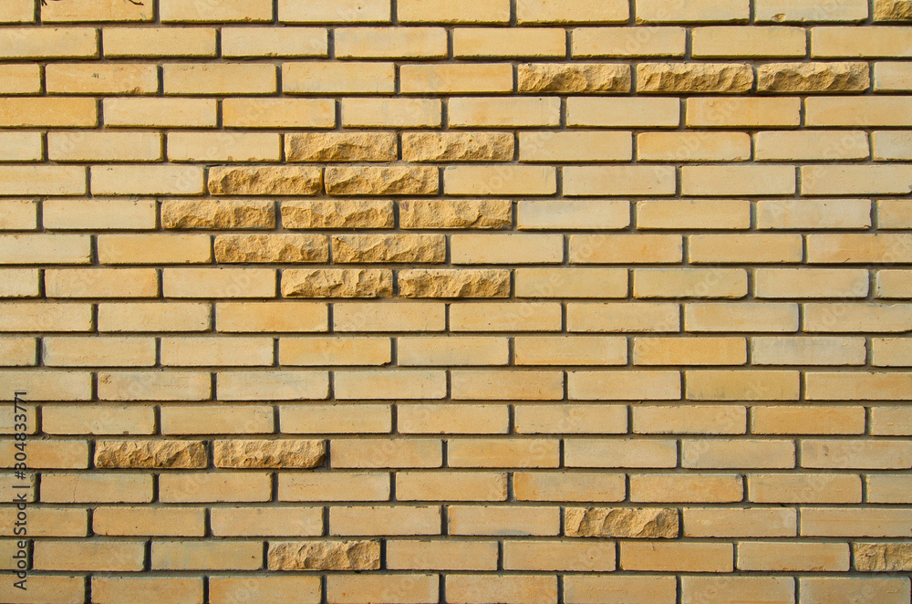 Naklejka premium Wall of yellow silicate brick. There are several decorative bricks with a chipped rustic edge. Background. Texture.