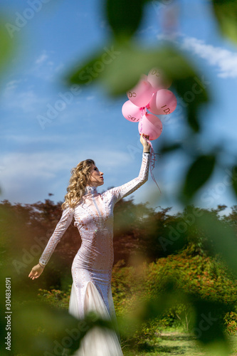 girl in a white long dress with pink balloons on the nature