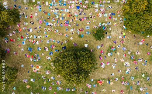 Top view of a crowd of people resting on the grass in a water park. People sunbathe and relax on rugs and wards on green grass.