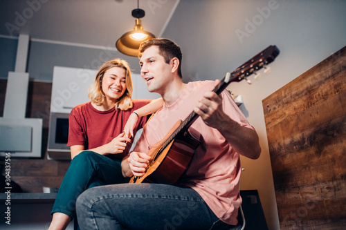 caucasian young male in casual wear sit with her blond short-haired girlfriend playing guitar for her and singing © alfa27