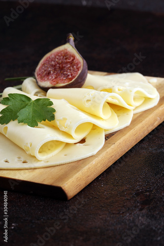 cheese slices on wooden tray with parsley. gauda cheese