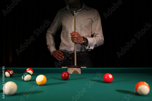 Sports game of billiards on a green cloth. Male player with a cue in his hands. Billiard balls with numbers on a pool table. Active leisure and entertainment. Billiards and billiard balls.