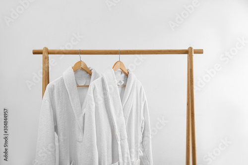 Fresh bathrobes hanging on rack near white wall