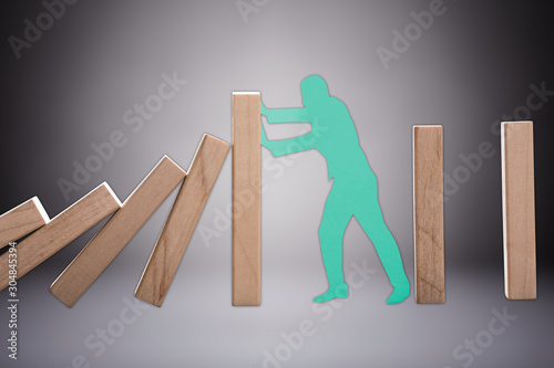Cut Out Human Figure Stopping The Wooden Domino To Fall