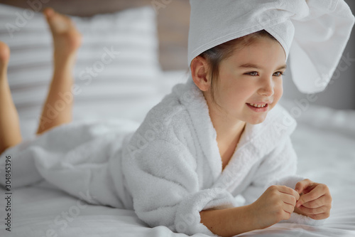 portrait of beautiful child wearing bathrobe and towel, lying on bed and smile. after shower