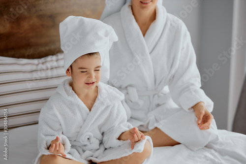 attractive female and child meditate after shower wearing bathrobe and towel, sit with closed eyes