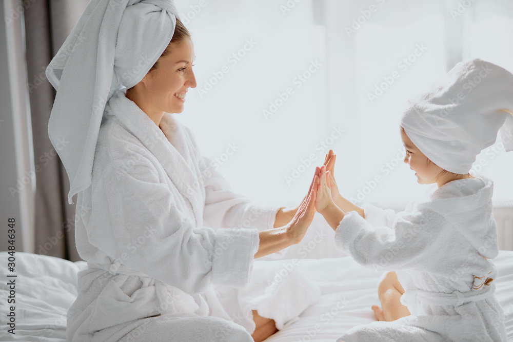 family game at home. friendly beautiful mother and her daughter sit clapping hands, play with each other, wearing white bathrobe and towel family game at home. friendly beautiful mother and her daughter sit clapping hands, play with each other, wearing white bathrobe and towel