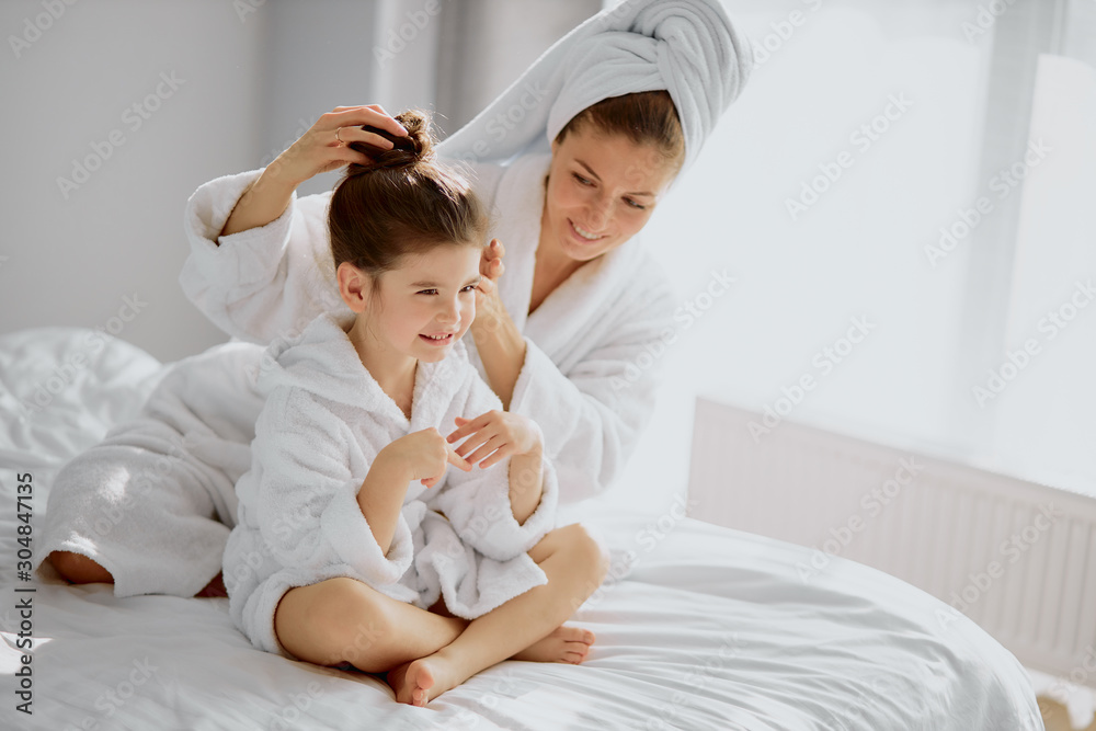 beautiful mother and daughter sit after shower, mom take care of little child after shower, isolated in white bedroom