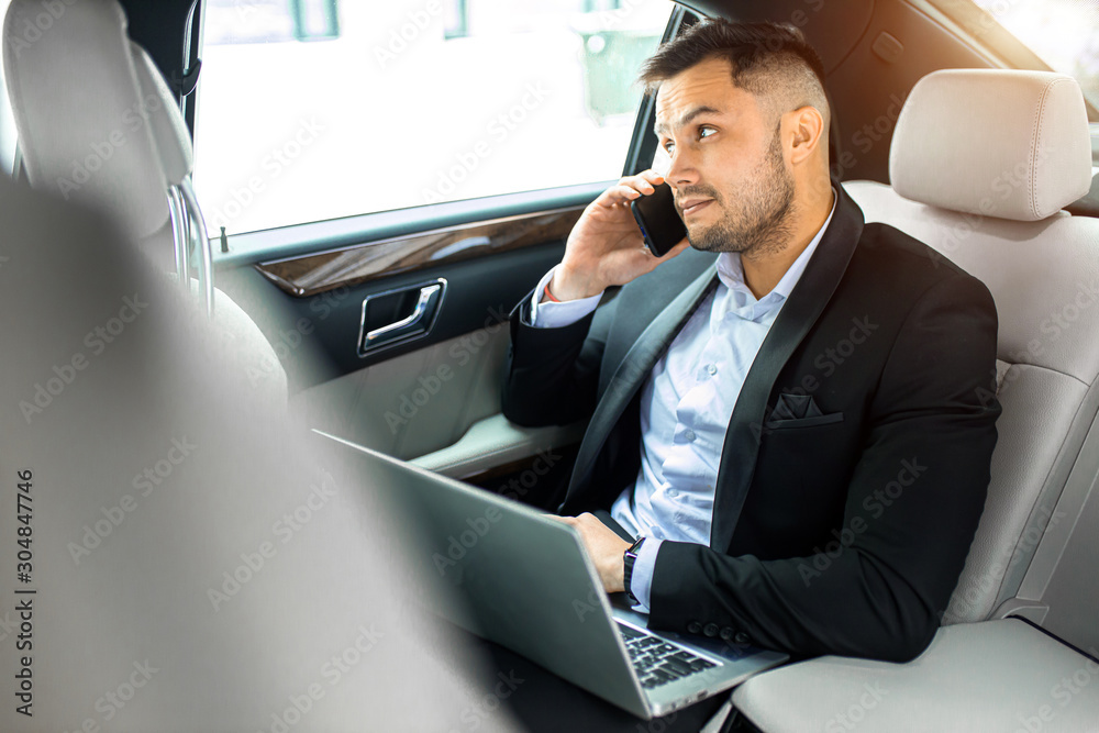 elegant young man with beard talking on phone, process of working in car, talk with his business colleague