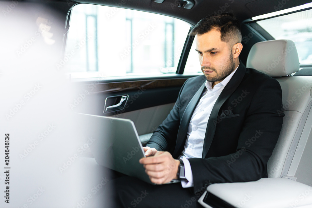 Confident man in tuxedo sit using laptop, working in car, man with beard
