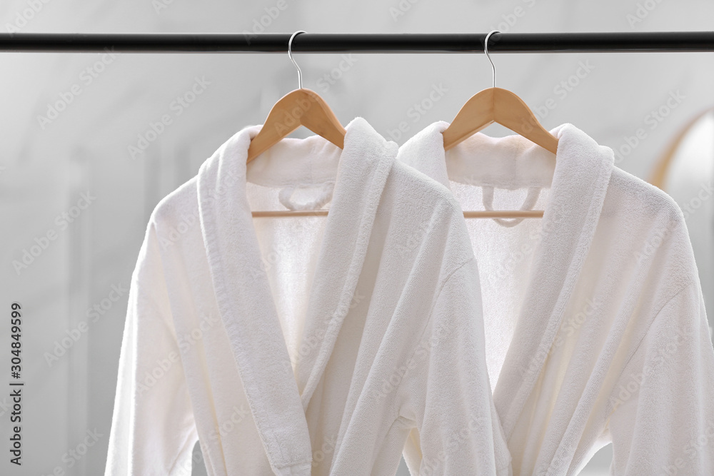 Fresh white bathrobes hanging on rack indoors - obrazy, fototapety, plakaty 