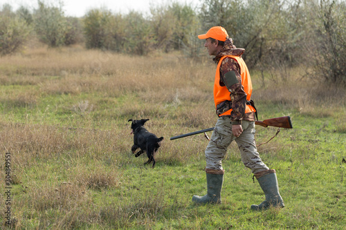 Hunting period, autumn season open. A hunter with a gun in his hands in hunting clothes in the autumn forest in search of a trophy. A man stands with weapons and hunting dogs tracking down the game. 