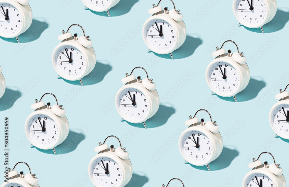 Pattern made of white alarm clocks on blue background. Trendy conceptual photo with open composition.