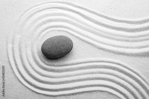 Grey stone on sand with pattern, top view. Zen, meditation, harmony