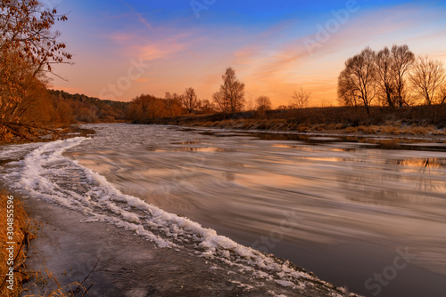 Fascinating sunset over freezing river and lonely tree