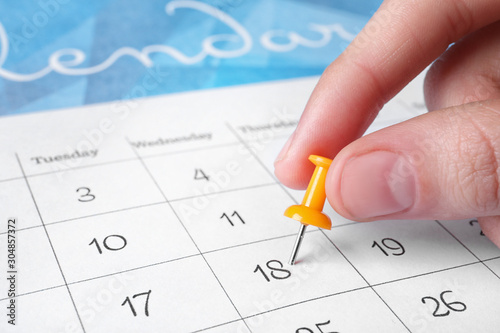 Woman marking date in calendar with drawing pin, closeup