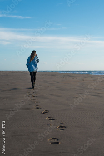 chica joven de espaldas paseando en la playa dejando sus huellas en la arena