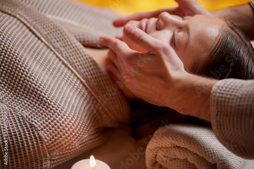 Young caucasian lady get reacreation massage of head, face. Lying down on desk for massages wearing bathrobe photo