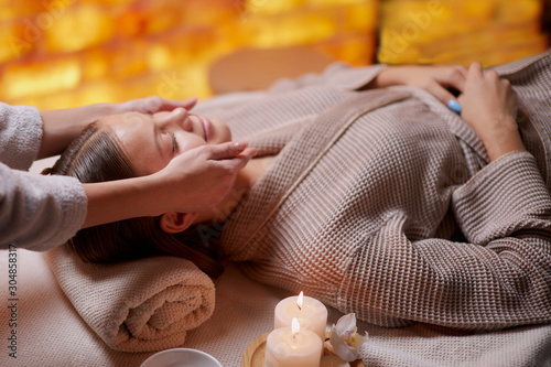 Canvas Print Beautiful woman in bathrobe getting facial massage by female hands in spa salon
