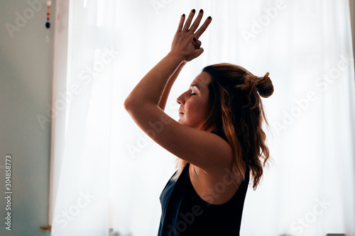 close up of a woman in a yoga position with closed eyes, clasped hands and raised arms performing the sun salutation flow - healthy lifestyle and meditation concept