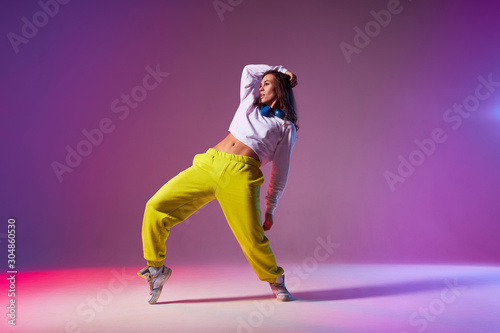 Cheerful energetic woman in casual outfit standing on tiptoe, bending back, showing sexy naked flat belly, performing dancing element on hip hop dance competition