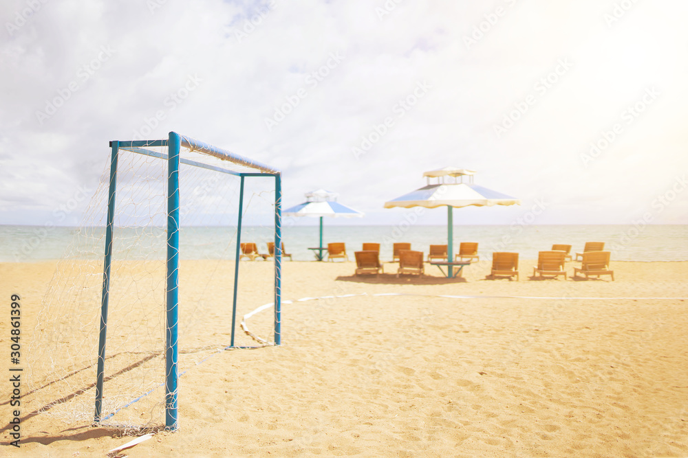 Football goal on the beach on the background of the sea and thighs with umbrellas Football goal on the beach on the background of the sea and thighs with umbrellas