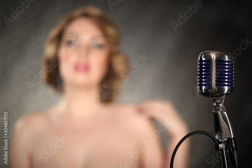 Girl singing in a retro microphone. Recording a clip in the studio of a professional singer. Close up face of singer with microphone on smoky gray background. The singer sings a song on stage.