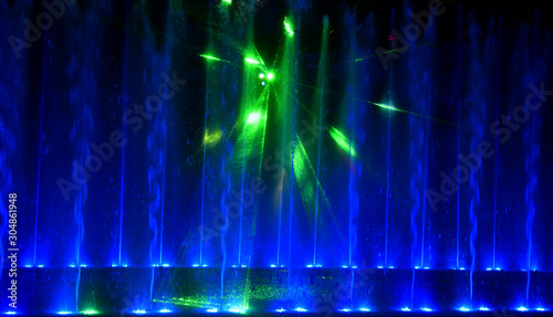 Colorful water fountains. Beautiful laser and fountains show. Large multi colored decorative dancing water jet led light fountain show at night. Dark background.