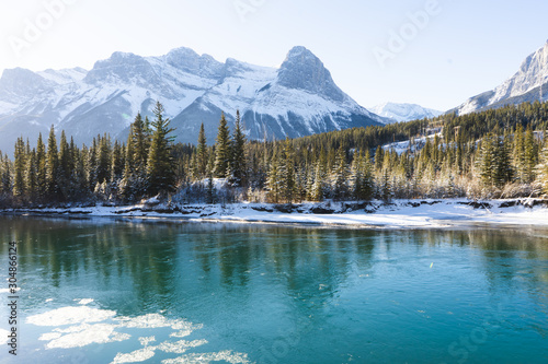 Fototapeta Naklejka Na Ścianę i Meble -  Canada Landscape. View of snow covered mountain scenery, Bow river and Three Sisters in winter. Beautiful sunny day in Canadian Rockies. Canmore, Alberta, Canada.