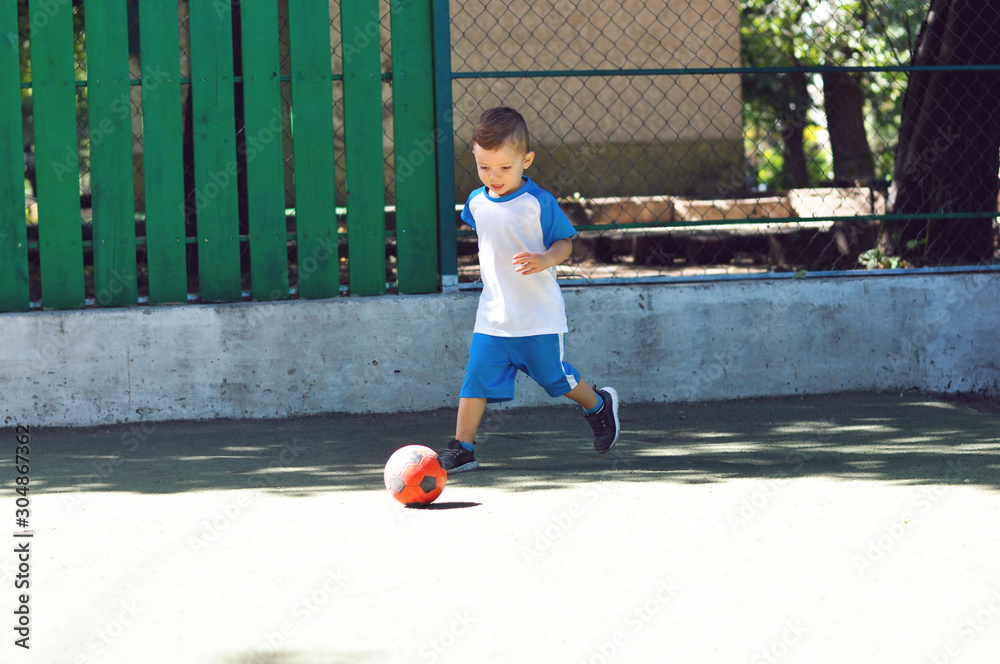 Little three year old boy in blue football uniform and with his red soccer ball Little three year old boy in blue football uniform and with his red soccer ball