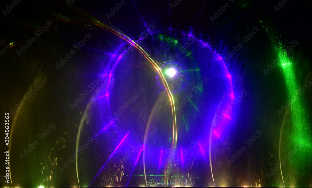 Fototapeta premium Colorful water fountains. Beautiful laser and fountains show. Large multi colored decorative dancing water jet led light fountain show at night. Dark background.