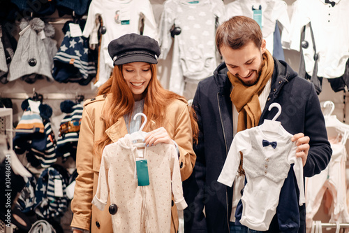 beautiful couple in love waiting for baby and looking for clothes for baby in clothes store