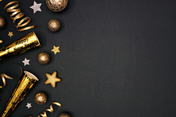 New Years Eve side border of glittery gold stars, streamers, decorations and noisemakers. Top view over a black background.