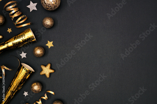 New Years Eve side border of glittery gold stars, streamers, decorations and noisemakers. Top view over a black background.