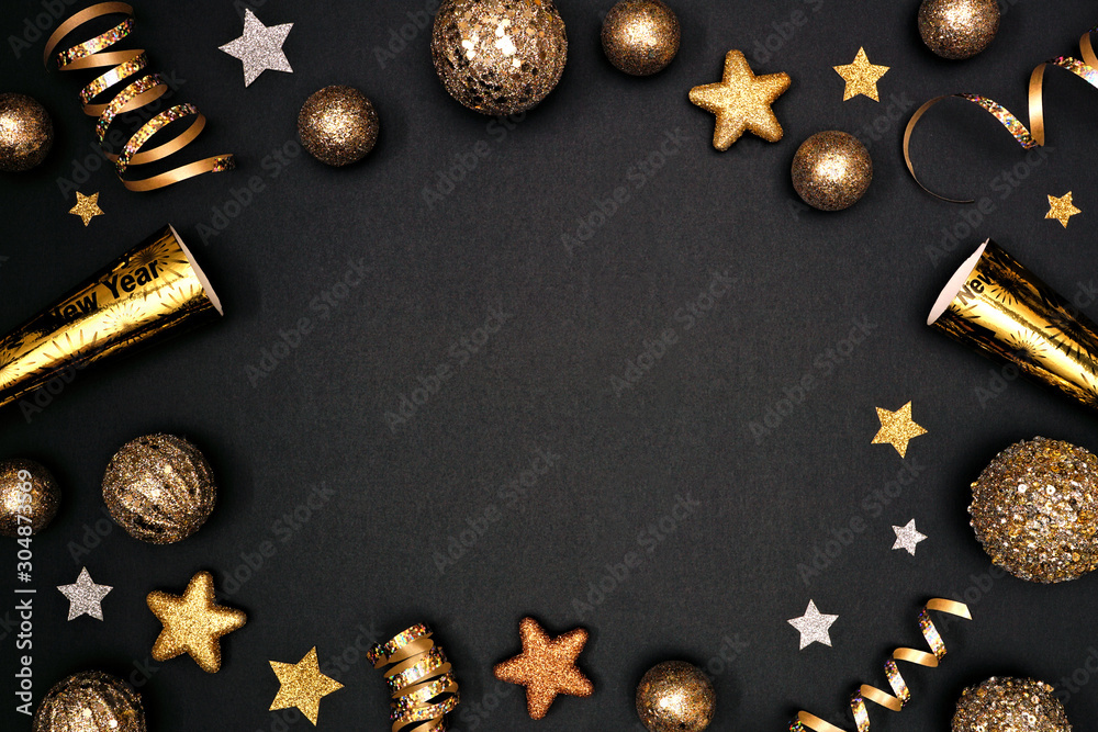 New Years Eve frame of glittery gold stars, streamers, decorations and  noisemakers. Above view on a black background. Stock Photo