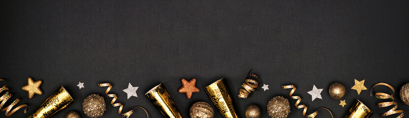 New Years Eve border banner of glittery gold stars, streamers, decorations and noisemakers. Above view over a black background.