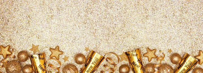New Years Eve border banner of gold decorations, steamers and noisemakers. Above view over a glittery gold background.