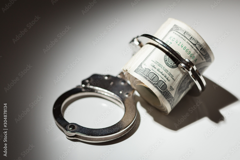 Handcuffs Locked on Roll of One Hundred Dollar Bills Under Spotlight Handcuffs Locked on Roll of One Hundred Dollar Bills Under Spotlight