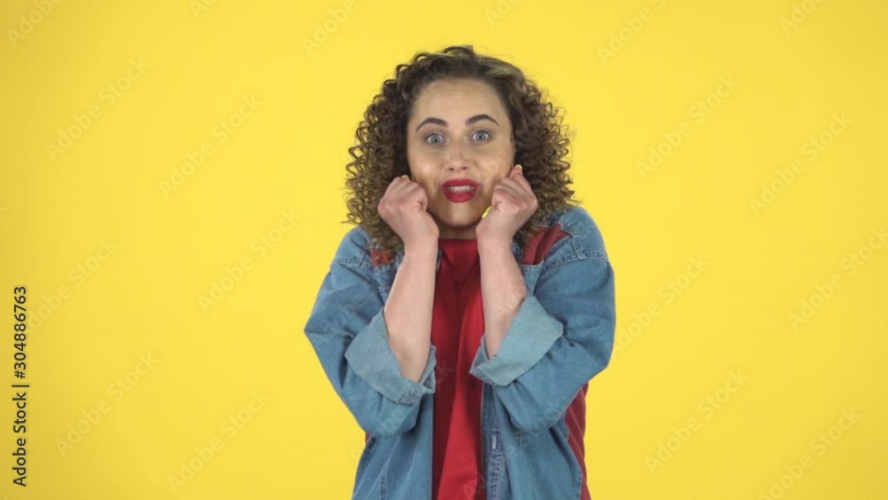 Very surprised girl with shocked wow face expression on yellow background at studio, slow motion.