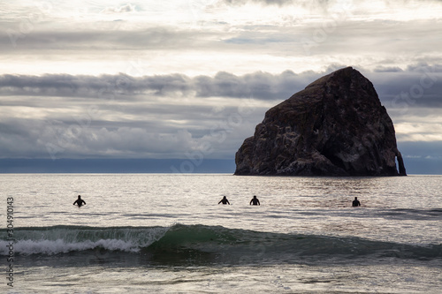 Pacific City, Oregon Coast, United States of America. Surfers waiting for the waves on the Ocean Coast during a cloudy summer evening with Chief Kiawanda Rock in background. photo