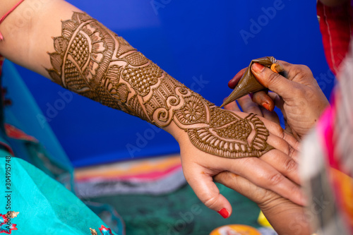 young woman mehendi artist painting henna on bride's hand before wedding day