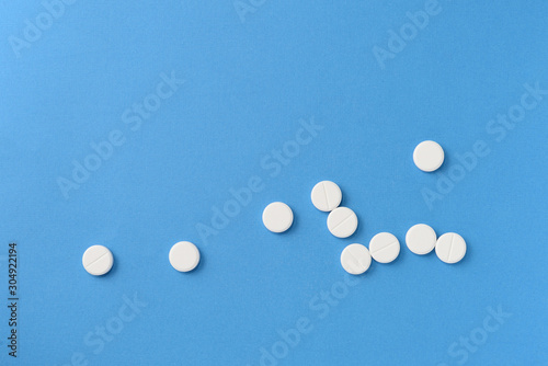 White round pills scattered on a blue background, top view. Medical pharmacy concept